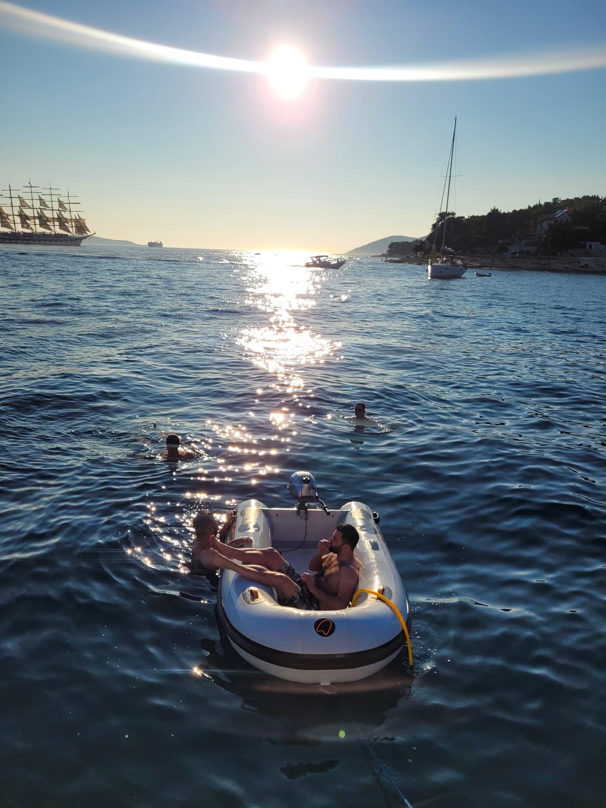 Driftawave team enjoying a sunset swim from an inflatable dinghy with a tall ship anchored in a Dalmatian bay.