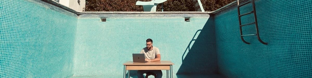 Remote work setup at a turquoise pool with a digital nomad working on a laptop, representing freedom from office cubicle life.