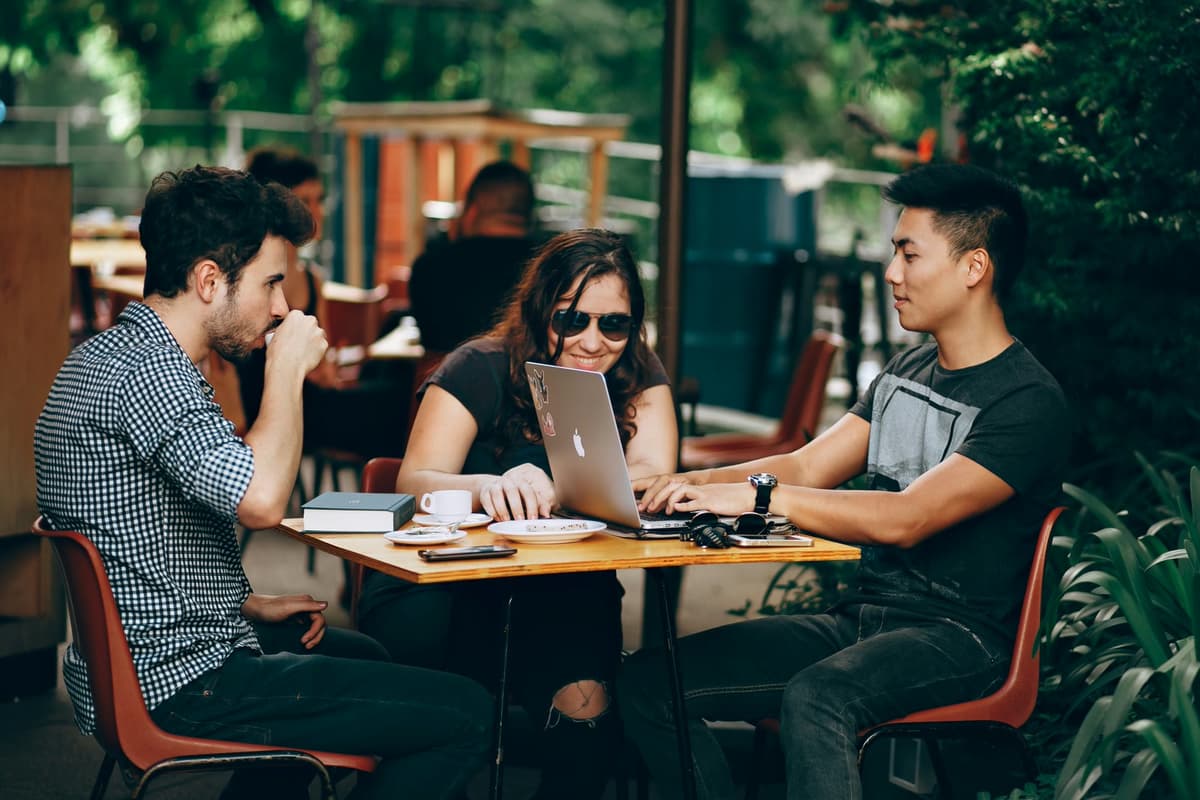 Distributed team members working together at an outdoor cafe table with laptops during a company offsite.