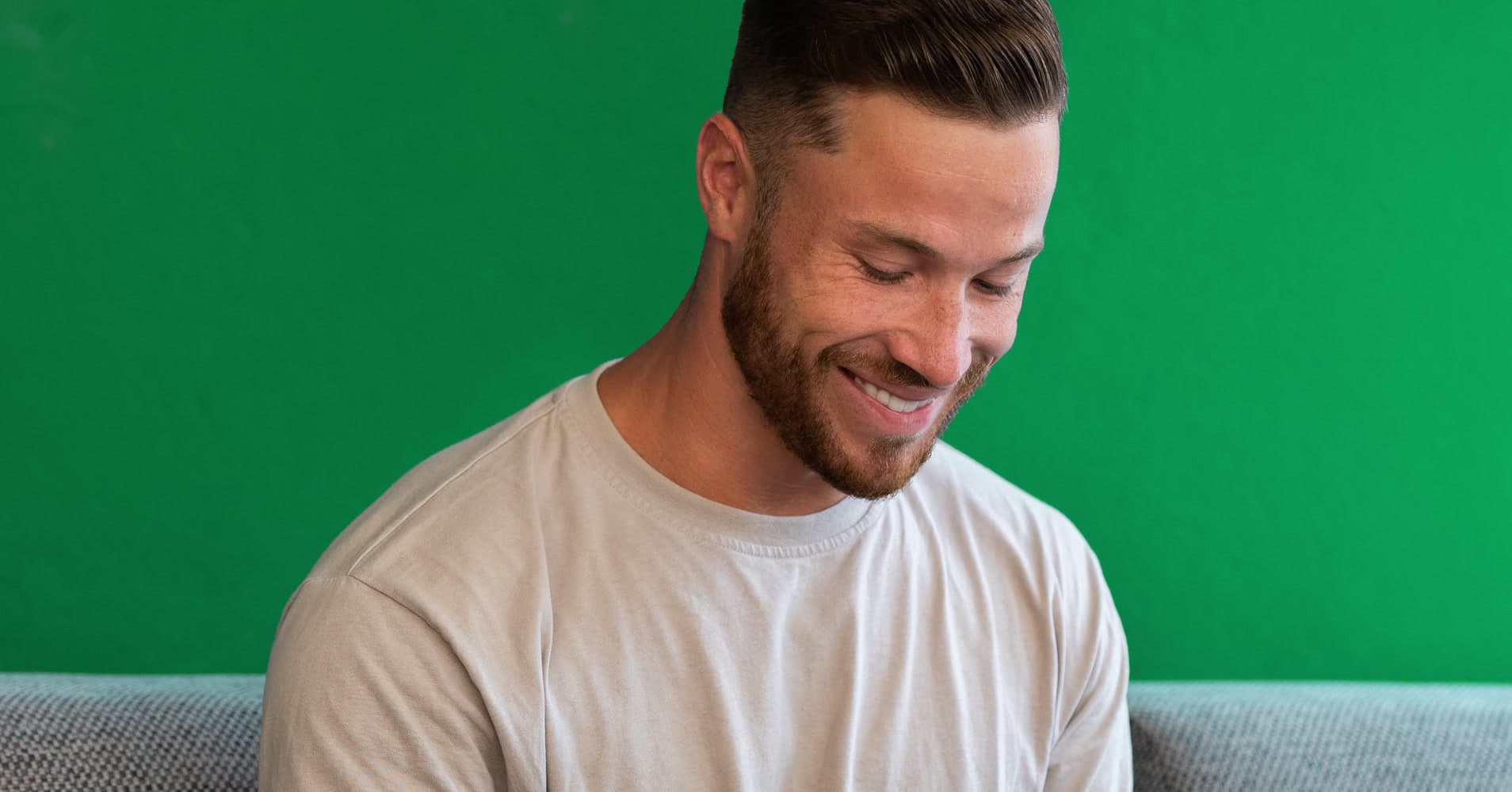 Digital nomad brand designer Youri van den Hurk working on a tablet from a couch against a green wall, remote work lifestyle in Portugal.