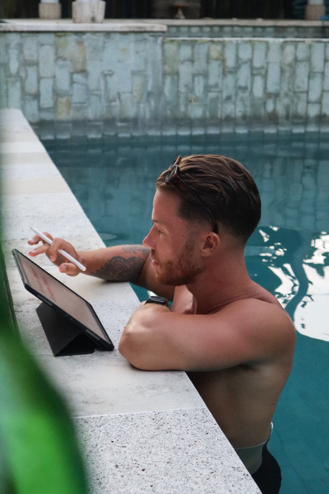 Digital nomad using a tablet in a pool, a flexible workation lifestyle combining work and leisure with Bali vibes.