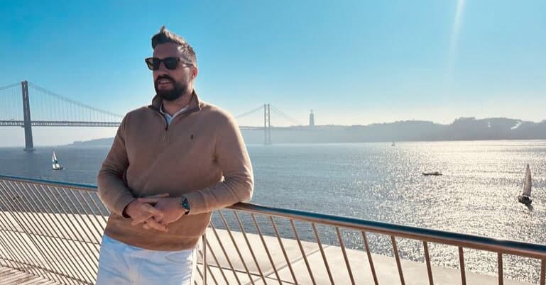 Alex Hernandez, co-founder of Jobgether, at the Lisbon waterfront with the 25 de Abril Bridge, embodying the remote work lifestyle and freedom.