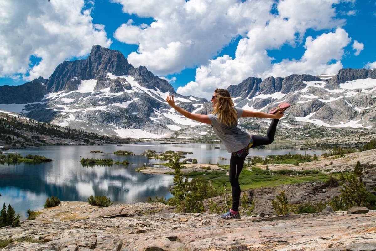 Burnout prevention expert Sally Clarke practicing yoga balance at an alpine lake, workplace wellbeing and mental clarity
