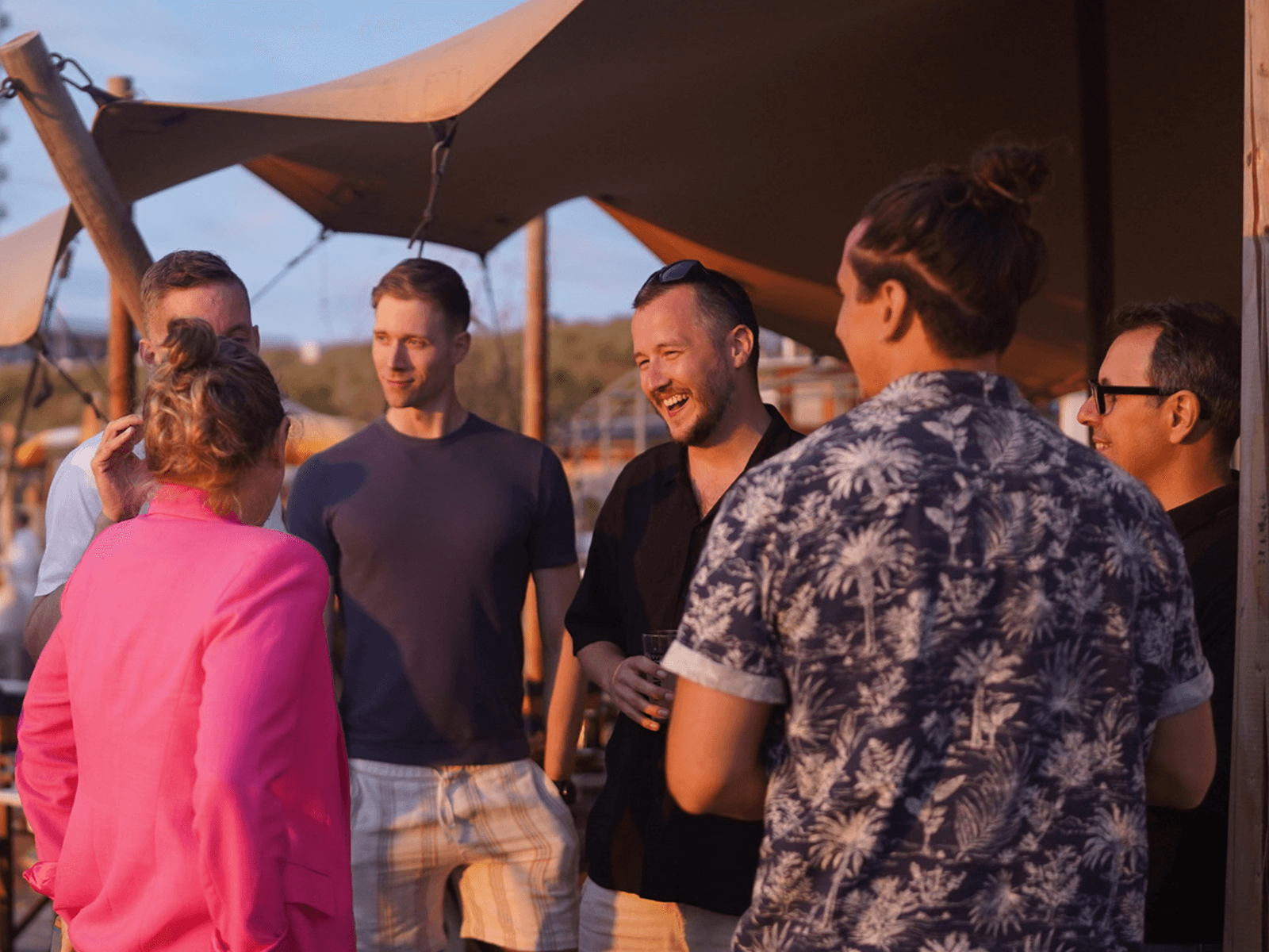 Team connecting over drinks under a stretch tent at golden hour during a Driftawave retreat