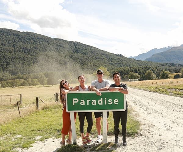 The team leaning on the Paradise road sign near Glenorchy, group travel day of a New Zealand team retreat