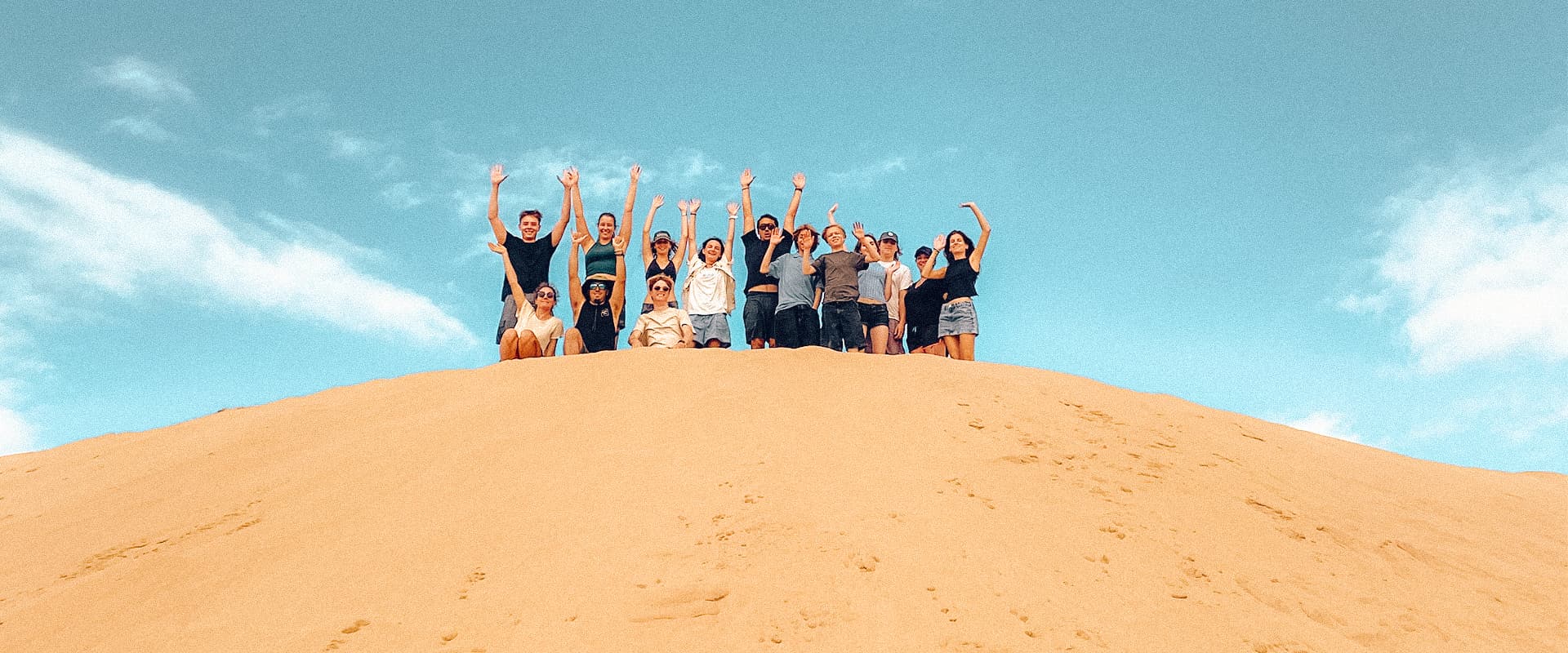 A remote team with arms up on the Gran Canaria dunes, the high point of a marketing team retreat