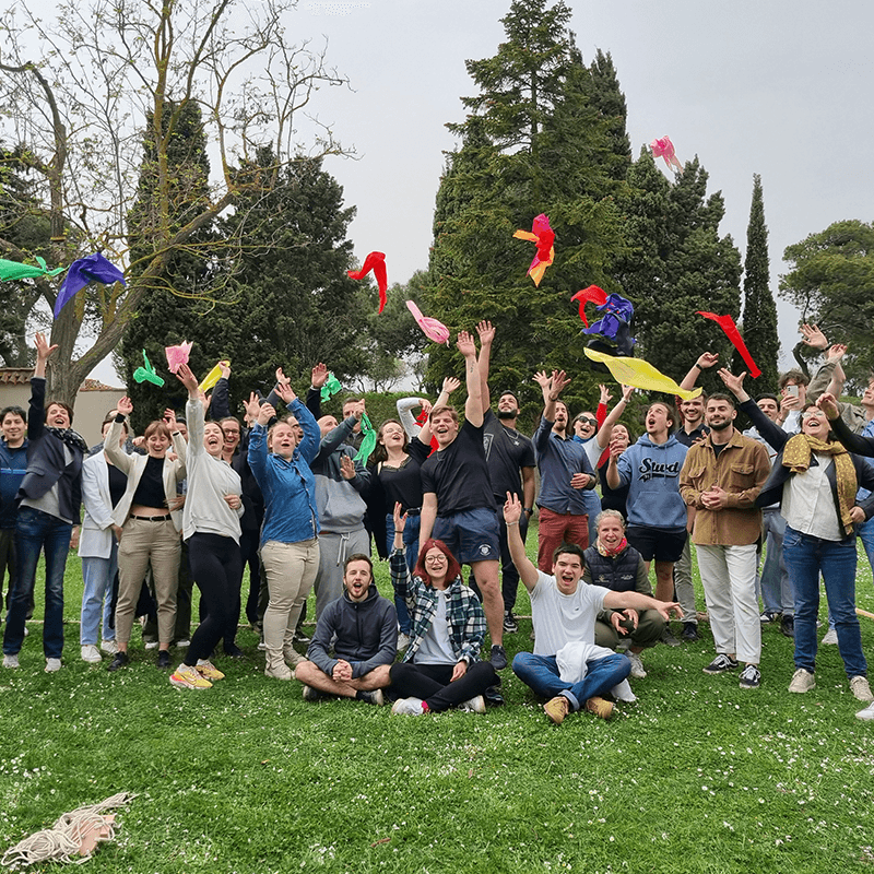 A remote team throwing coloured scarves in the air, the group photo of a teambuilding team retreat